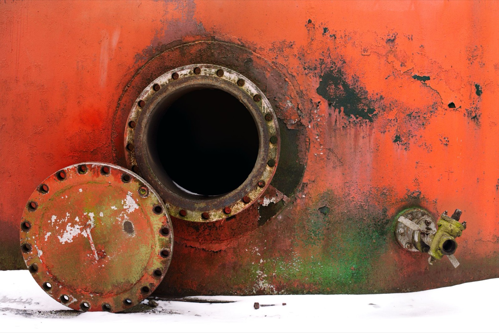 An open tank manway with its cover lying in the snow